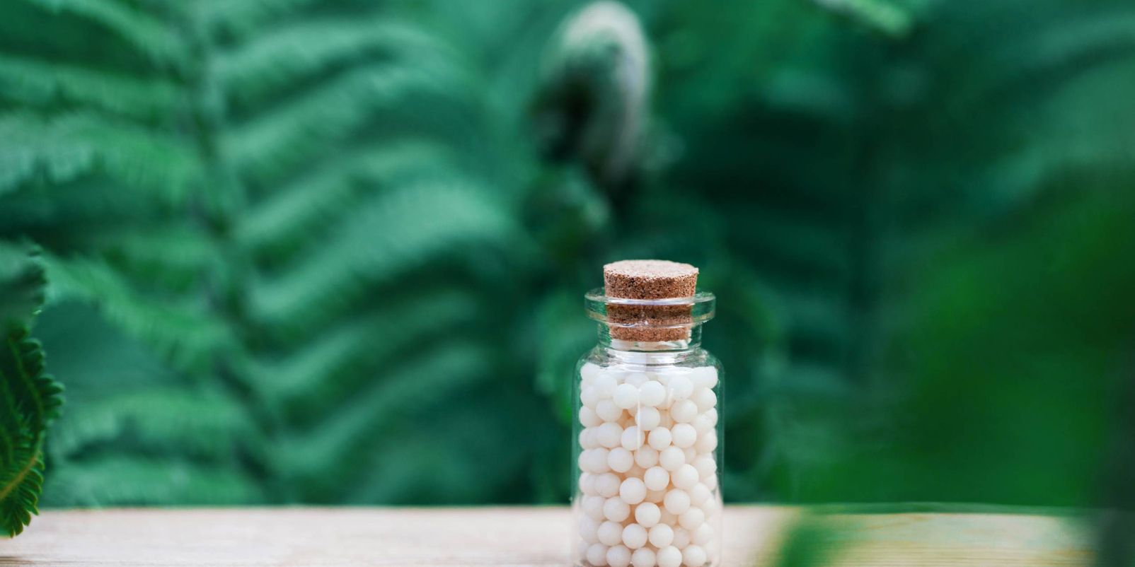 Bottles of homeopathic globules on green fern background. Homeopathy medicine.