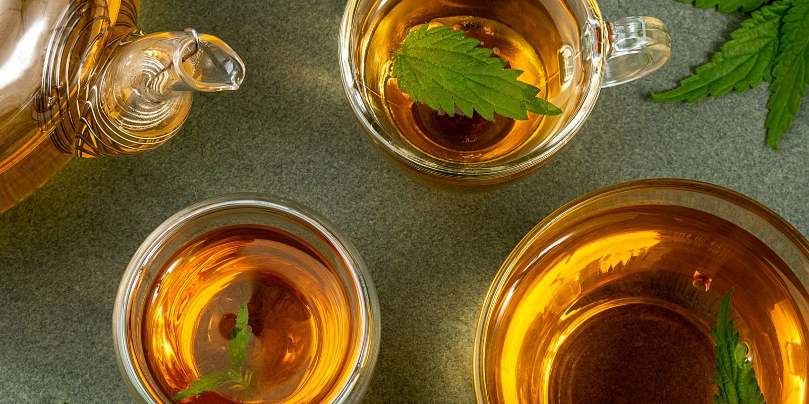 Cups of herbal tea, transparent teapot and nettle leaves on green background. Calming drink concept. Top view Flat lay.