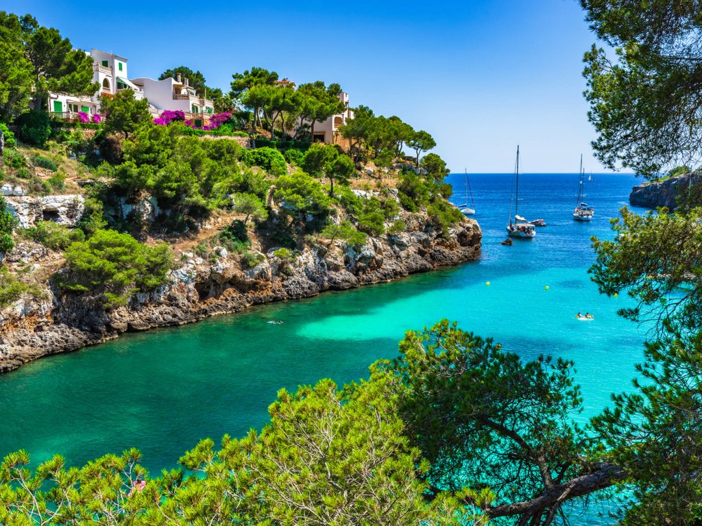 Bucht mit türkisfarbenem Wasser, Bäumen und Booten auf dem Wasser