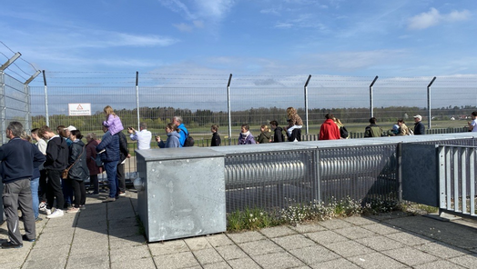 Aufnahme der Besucherterasse vom Bodensee-Airport Friedrichshafen. Zu sehen sind einige Menschen die vor einem Zaun stehen und auf das Vorfeld schauen