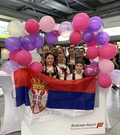 Kinder des serbischen Kulturvereins Friedrichshafen in einem großen Polaroid-Rahmen mit einer serbischen Flagge in der Hand