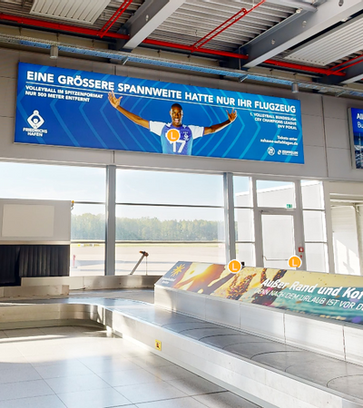 Gepäckband am Flughafen mit einem großen Werbebanner an der Wand
