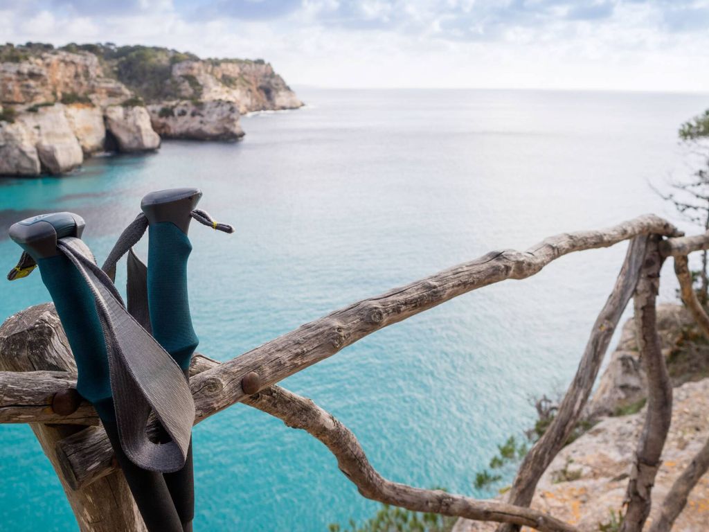 Blaues, weites Meer in einer Bucht im Hintergund, Wanderstöcke im Vordergrund
