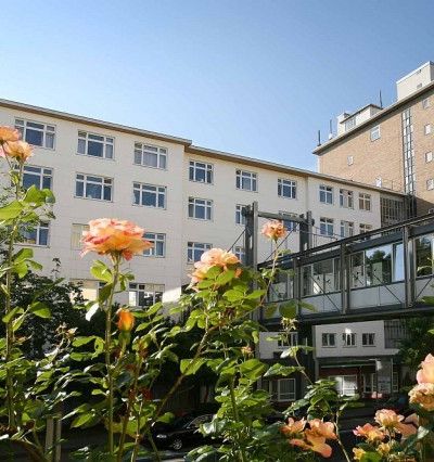 Blick auf die neurologische Klinik Westend. Vorne im Bild sind Rosen im hellen rosa zu sehen.
