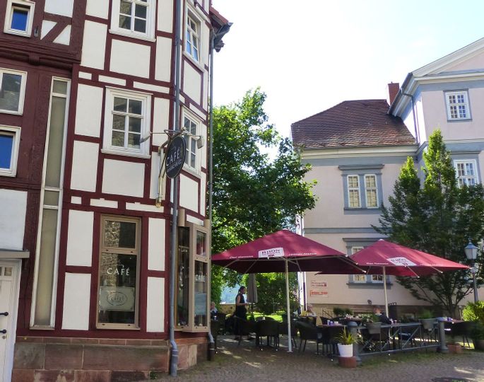 Außenaufnahme des "Café am Kirchplatz" in der Alstadt von Bad Wildungen mit Sitzbereich draußen. Dort befinden sich bei sonnigem Wetter Menschen auf der Freifläche.