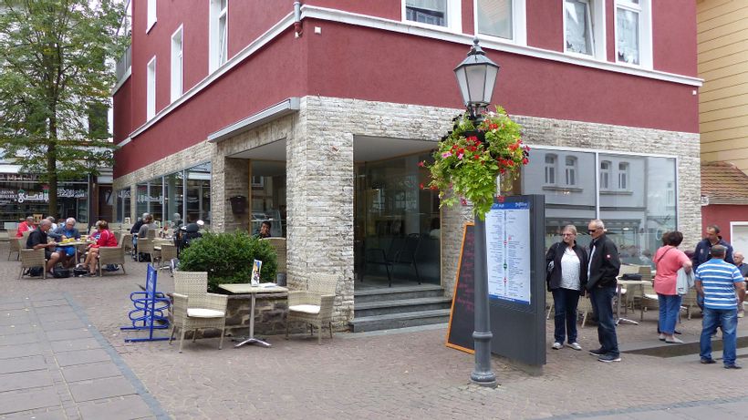 Blick auf den Eingang des Cafe unterm Kirchplatz mit Menschen, die Kaffee und Kuchen genießen.