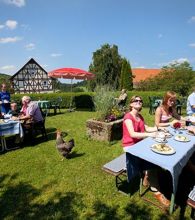 Garten des Dülfershof mit Menschen, die an Tischen sitzen.