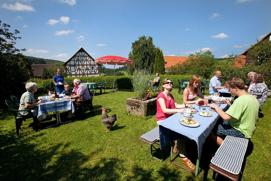 Garten des Dülfershof mit Menschen, die an Tischen sitzen.