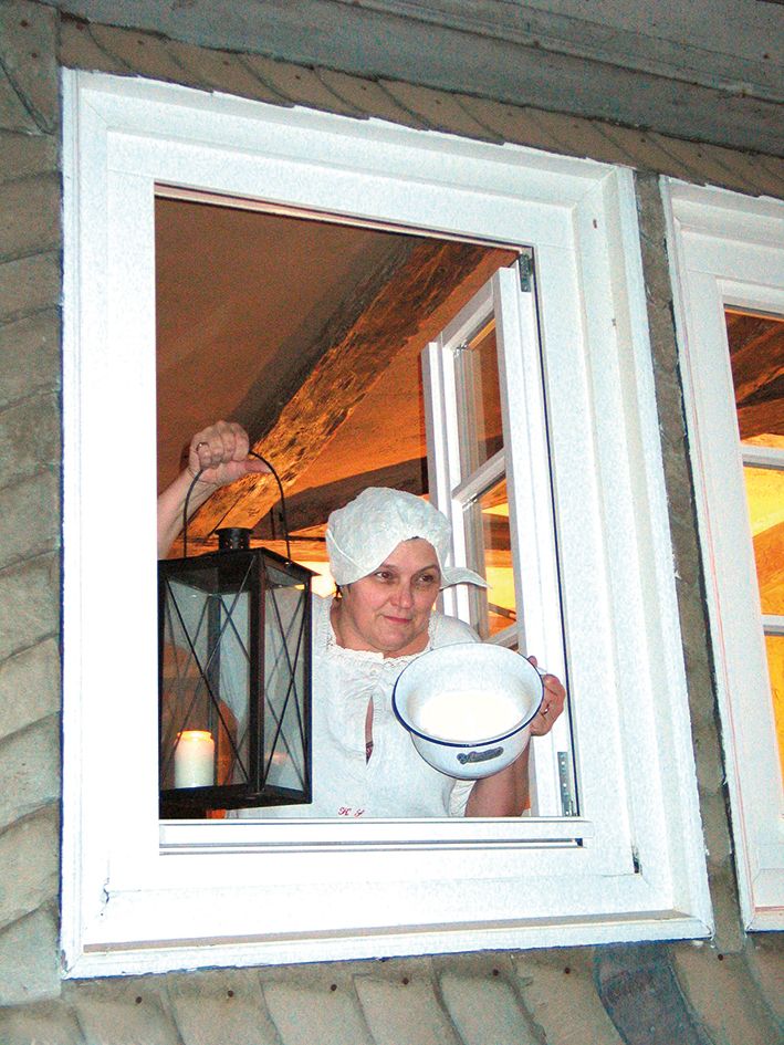Bild der Gästeführerin Ute Ahrend, die mit einer Laterne und einem Topf in der Hand aus einem Fenster schaut.