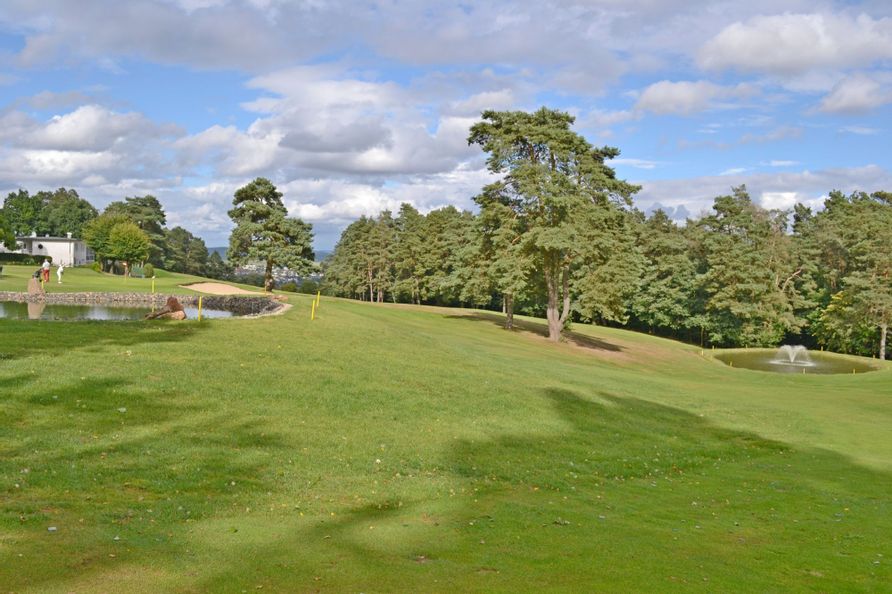 Blick auf einen Golfplatz der mit Bäumen, Sandbunkern und Teichen durchzogen ist