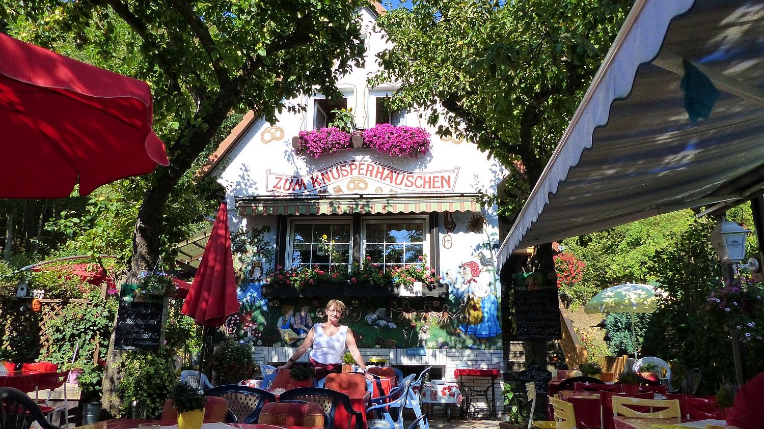 Blick auf das bemalte Haus des Knusperhäuschen und einer Frau, die davor sitzt, in Reitzenhagen.