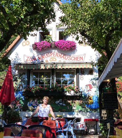 Blick auf das bemalte Haus des Knusperhäuschen und einer Frau, die davor sitzt, in Reitzenhagen.
