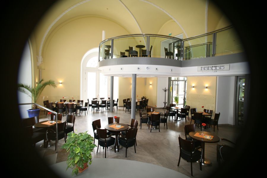 Innenbereich des Quellencafes in Bad Wildungen. Zu sehen ist eine Empore mit Tischen und Stühlen sowie der untere Bereich mit Tischen und Stühlen.