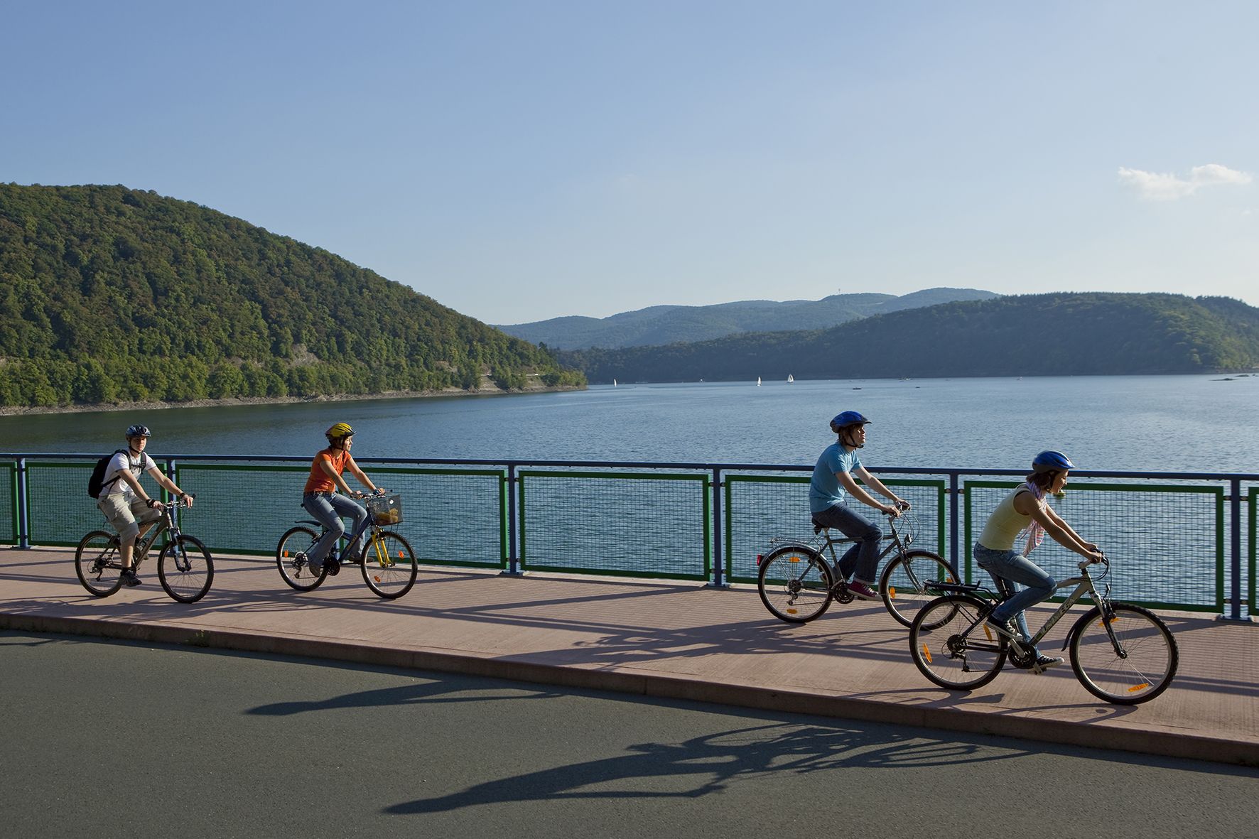 Vier Fahrradfahrer fahren auf einem Bürgersteig entlang des Edersees.