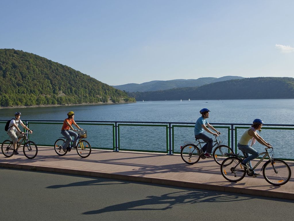 Vier Fahrradfahrer fahren auf einem Bürgersteig entlang des Edersees.