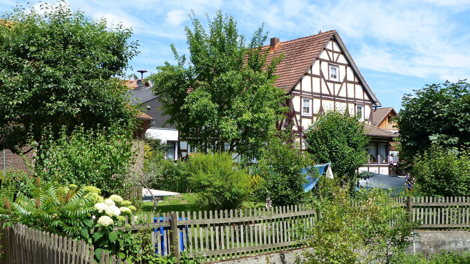 Blick auf ein Fachwerkhaus in Hüddingen mit einem Garten voller grüner Bäume und Sträucher.