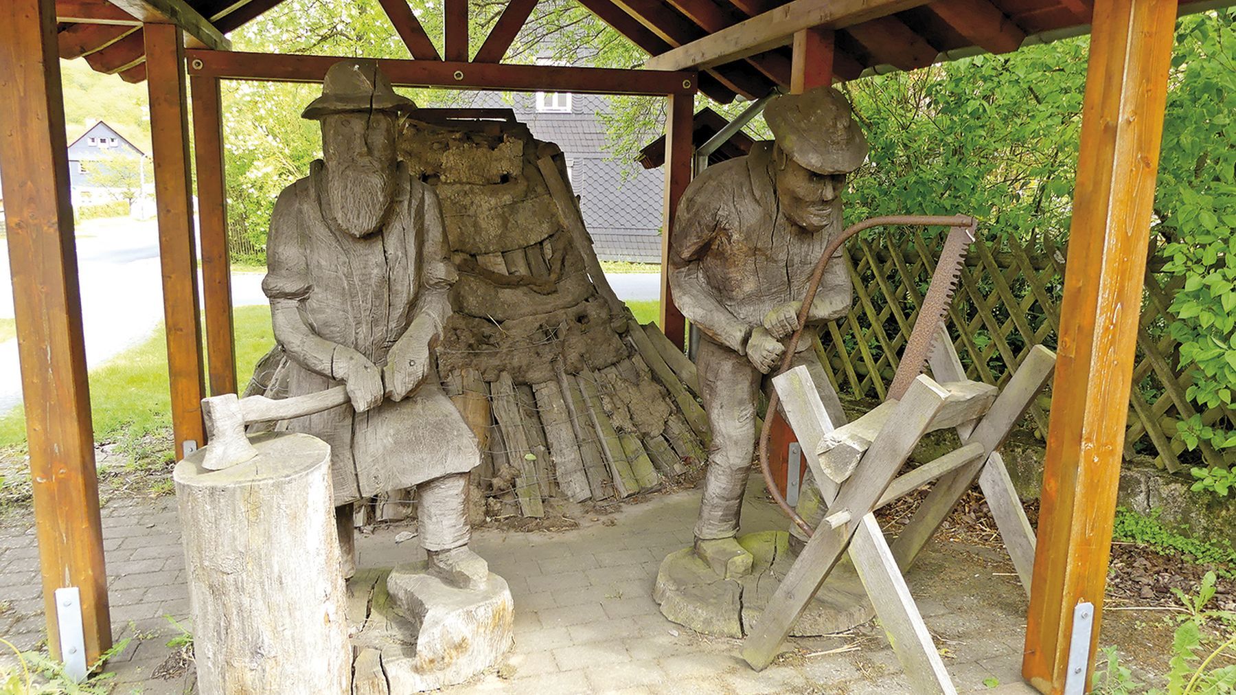 Holzfiguren in Hundsdorf. Ein Baumfäller mit einer Axt und ein Mann mit einer Säge, der Holz durchsägt.