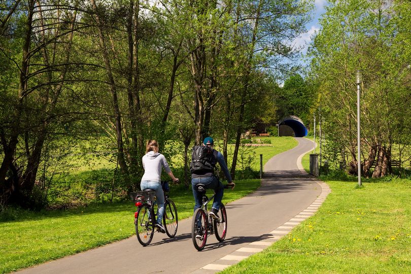 Zwei Radfahrer fahren durch den Bad Wildunger Kurpark auf den Quellen-Tunnel zu
