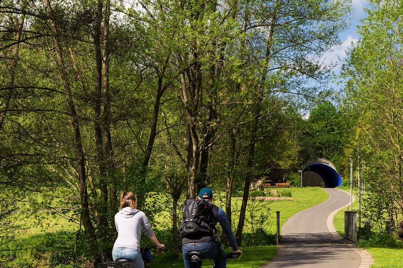 Zwei Radfahrer fahren durch den Bad Wildunger Kurpark auf den Quellen-Tunnel zu