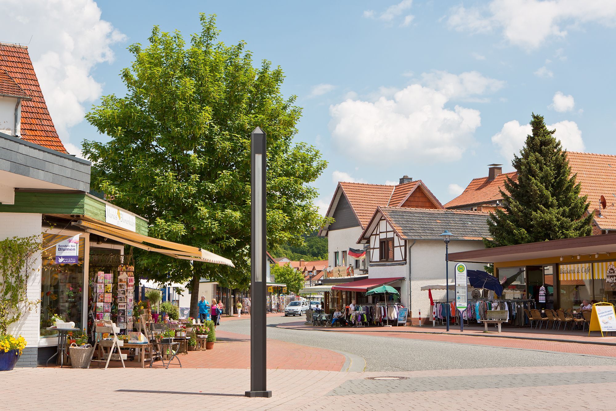 Blick in die Hauptstraße im Stadtteil Reinhardshausen mit offenen Geschäften, wie einem Blumenladen, Bekleidungsgeschäft und Bäckerei. Auf der Straße bummeln die Menschen bei sommerlichen Temperaturen.