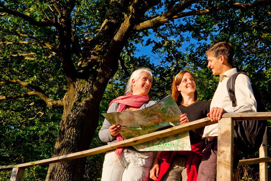 3 Personen die mit einer Karte an einem Holzgeländer stehen und sich gegenseitig anlächeln.