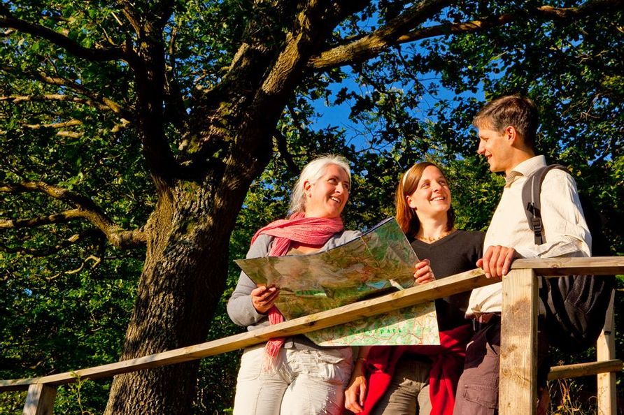 3 Personen die mit einer Karte an einem Holzgeländer stehen und sich gegenseitig anlächeln.