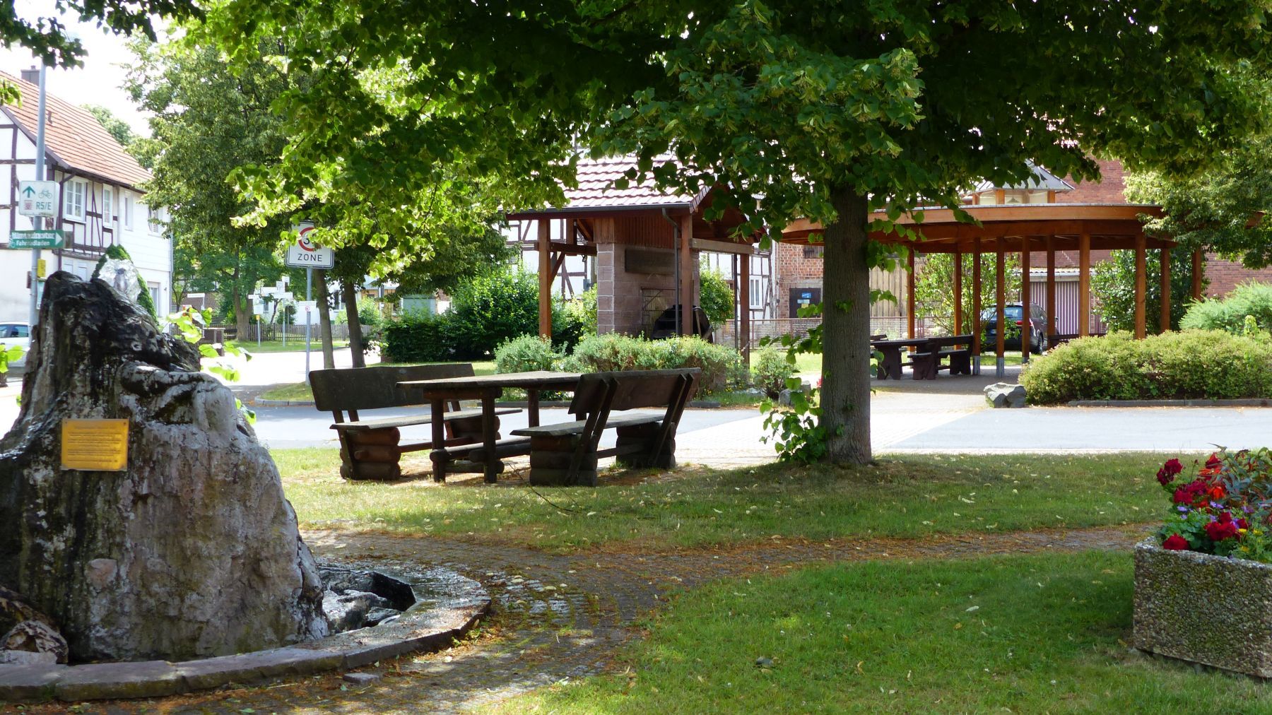 Blick auf die Dorfmitte von Wega mit Tischen und Bänken und einem Baum in der Mitte.