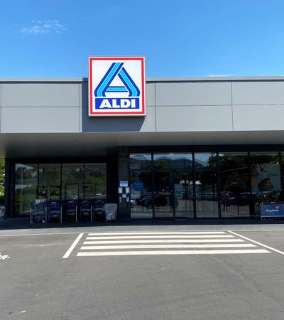Außenansicht des Eingangs von Aldi. Vor dem Gebäude sind Parkplatze und neben dem Eingang die Einkaufswagen zu sehen.