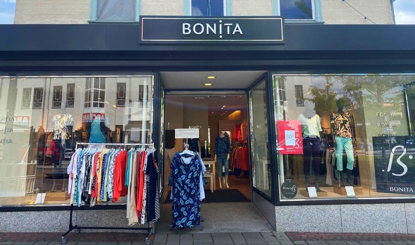 Außenansicht des Eingangs vom Damenbekleidungsgeschäft bonita. Links vom Eingang steht ein Ständer mit Kleidungsstücken.