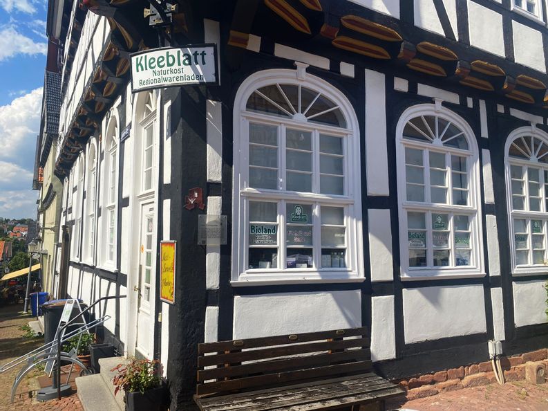 Außenansicht des Eingangs vom Regionalwarenladen Kleeblatt. Das geschäft befindet sich in einem Fachwerkhaus. Vor dem Eingang sind drei Stufen nach oben und rechts neben dem Eingang befindet sich eine Bank.