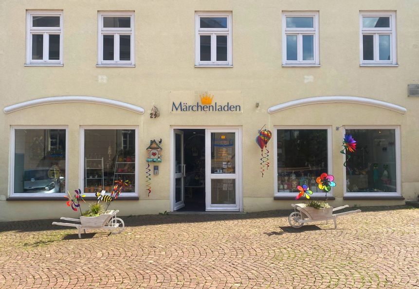 Außenansicht des Eingangs des Märchenladens in der Altstadt. Links und rechts vom Eingang stehen zwei Schubkarren aus Holz, die mit kleinen Windrädern und grünen Pflanzen bestückt sind.