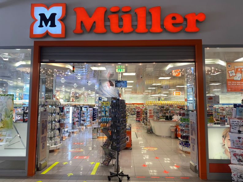 Offener Eingangsbereich von Müller mit Blick in das Geschäft in der Fürstengalerie. Vor dem Eingang steht ein Ständer mit Ansichtskarten.