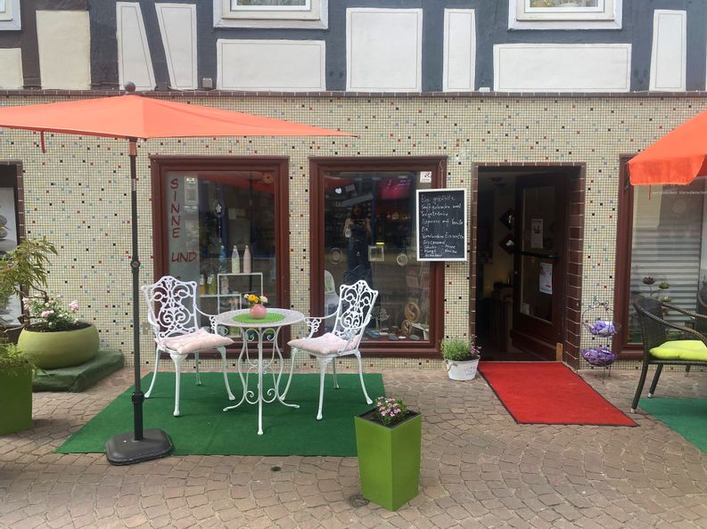 Außenansicht des Eingangs von Sinne und Seele in der Altstadt. Vor dem Eingang sind Tische, Stühle ein roter Sonnenschirm und Blümchen zu sehen.