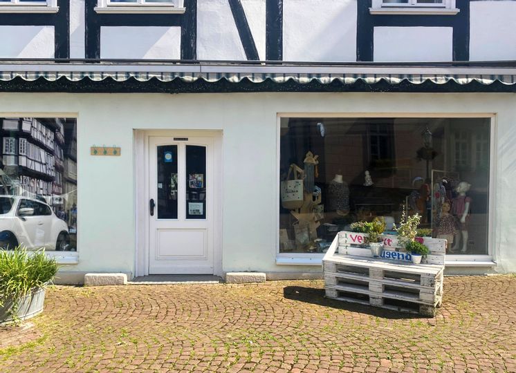 Außenansicht des Eingangs vo Verflixt und Zugenäht. Rechts neben dem Eingang stehen weiße Holzpaletten, auf denen Pflanzen stehen.