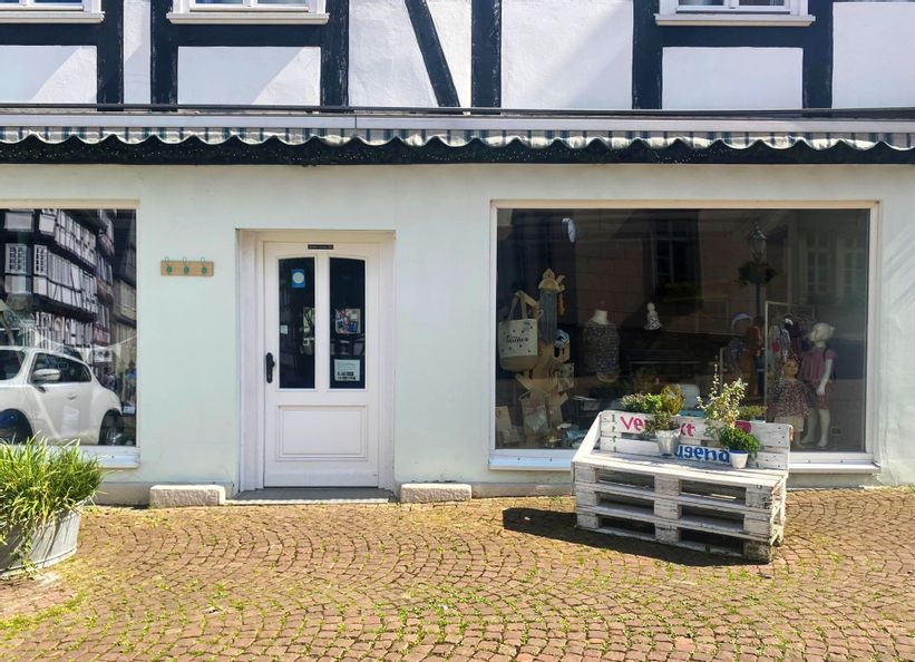 Außenansicht des Eingangs vo Verflixt und Zugenäht. Rechts neben dem Eingang stehen weiße Holzpaletten, auf denen Pflanzen stehen.