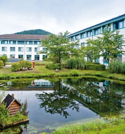 Blick auf das Gebäude sowie einen Teil des Außengeländes der Mediclin Kliniken Bad Wildungen. In der Gartenanlage sind ein Teich, Wiese und Bäume zu sehen.