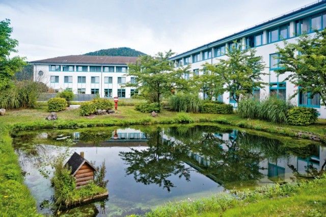 Blick auf das Gebäude sowie einen Teil des Außengeländes der Mediclin Kliniken Bad Wildungen. In der Gartenanlage sind ein Teich, Wiese und Bäume zu sehen.