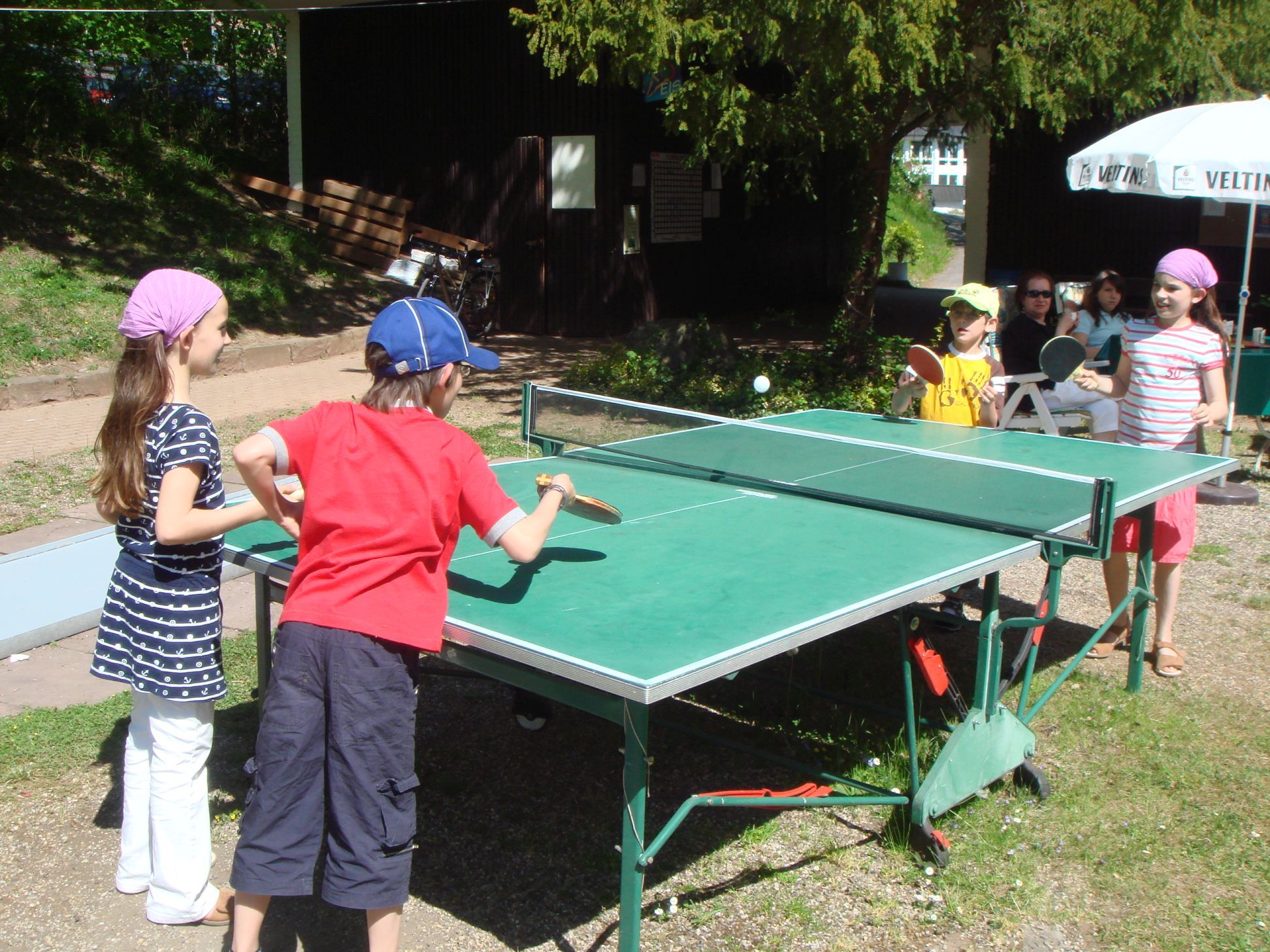 4 Kinder spielen Tischtennis an einem sonnigen Tag