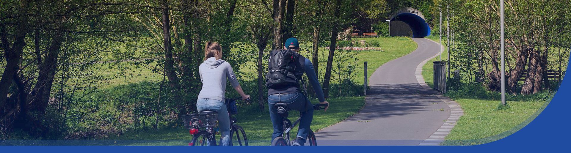 Zwei Radfahrer fahren durch den Bad Wildunger Kurpark auf den Quellen-Tunnel zu