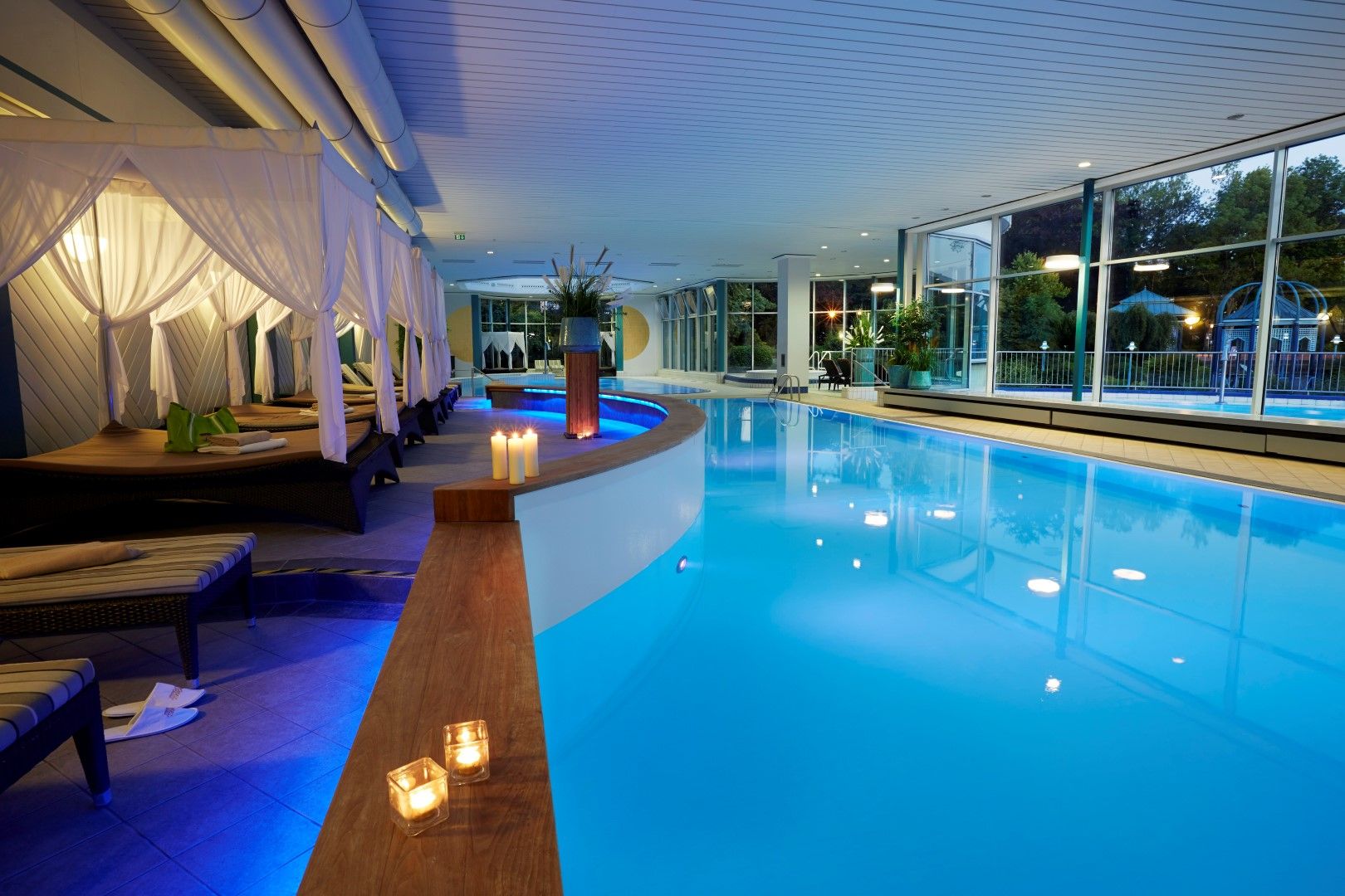 QuellenTherme im Goebel's Hotel AquaVita - Innenbereich mit Pool, Liegen, Betten und Kerzen bei Dämmerung.