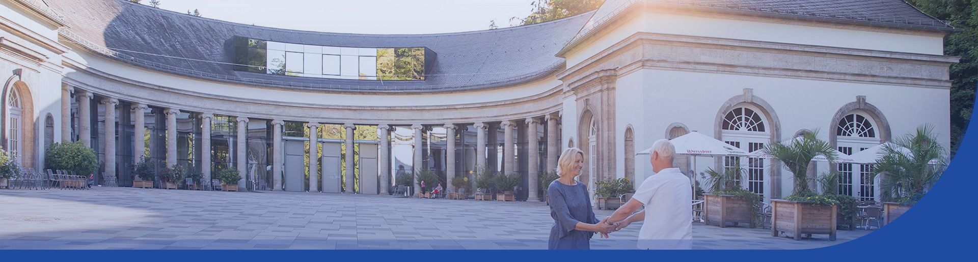 Blick auf die Wandelhalle im Bad Wildunger Kurpark. Im Vordergrund, zwei ältere Personen, die sich an den Händen halten