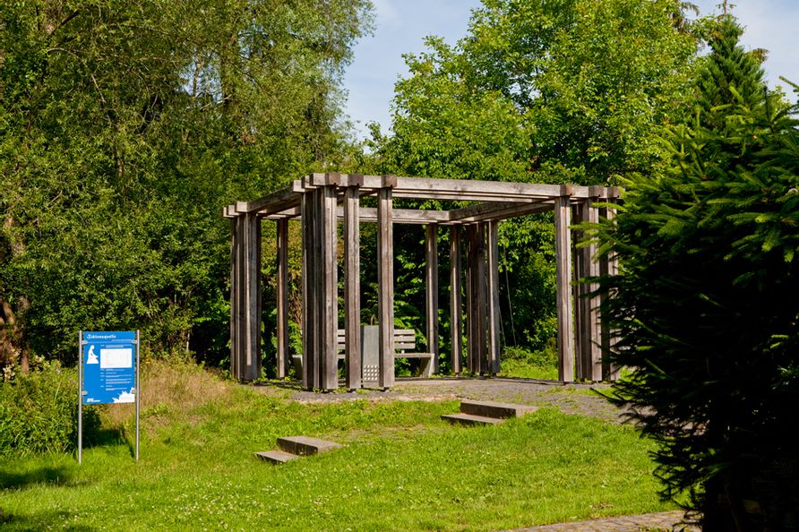 Blick auf die Schlossquelle im Kurpark Bad Wildungen umgeben von grünen Bäumen bei sonnigem Wetter.