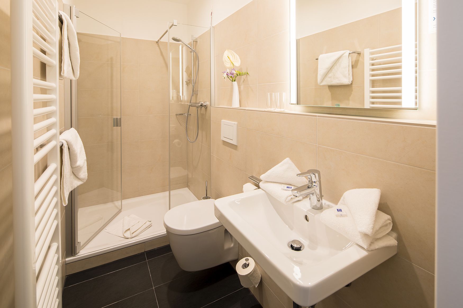 Gesundheitszentrum Helenenquelle. Blick in ein Badezimmer mit Dusche, Waschbecken, Toilette und weißen Handtüchern.