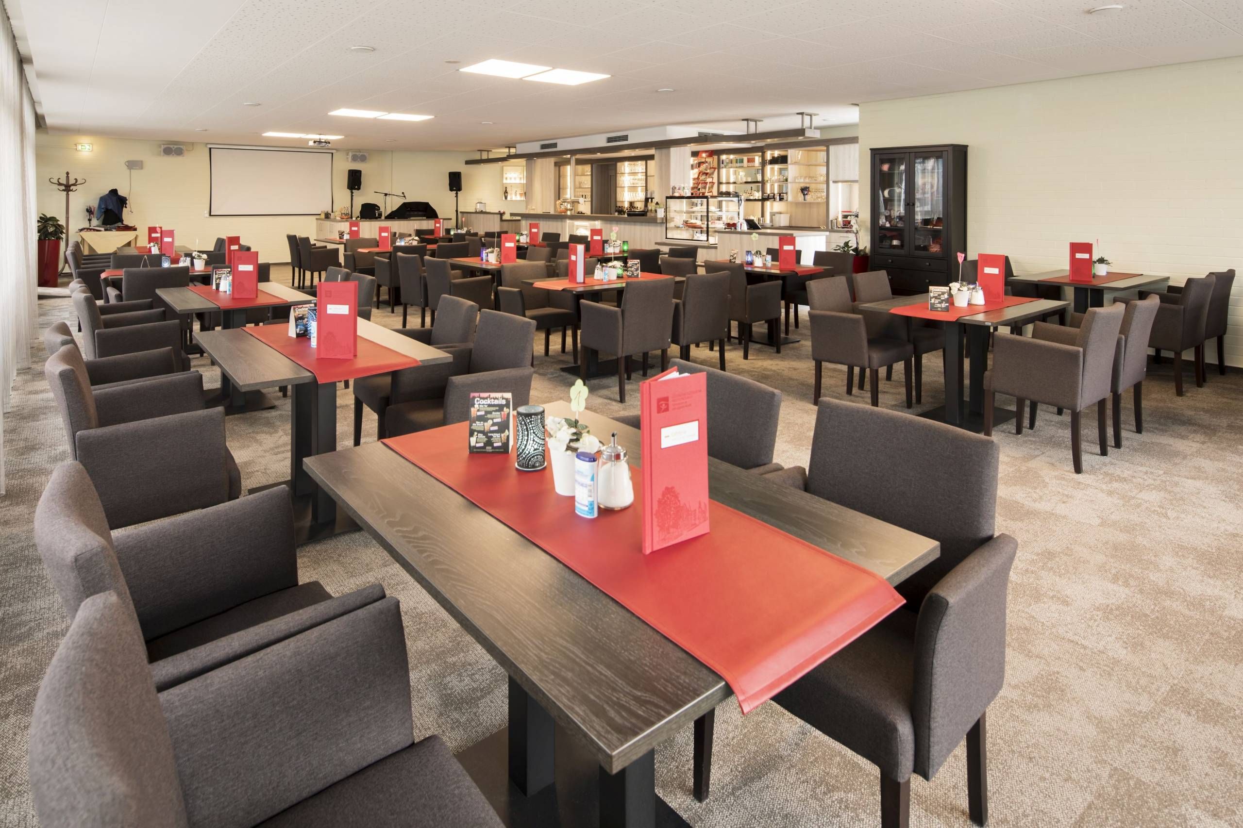 Gesundheitszentrum Helenenquelle Bad Wildungen Blick in das Restaurant mit vielen Tischen und Stühlen. Auf den Tischen sind rote Tischläufer, rote Karten, Zucker, Blümchen und Kerzen. Im Hintergrund ist ein Tresen zu sehen.