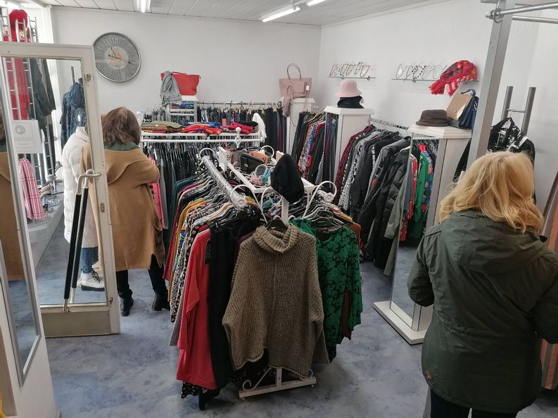 Blick in das Geschäft Kurvenreich. Zu sehen sind drei Frauen, die sich im Geschäft umschauen sowie Kleiderstände an den Seiten und in der Mitte des Raumes. Links auf dem Bild ist die offene Eingangstür zu sehen.