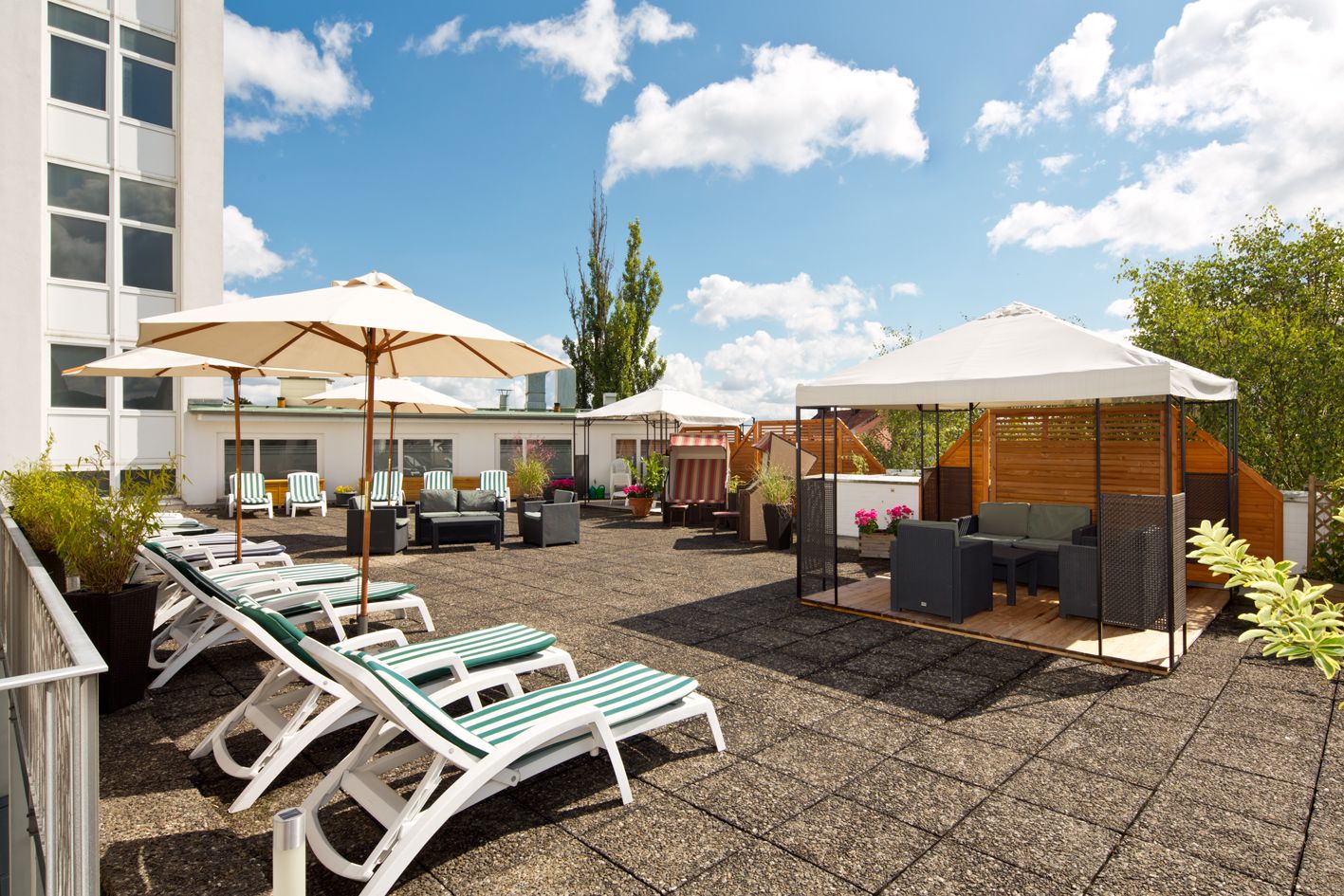 Gesundheitszentrum Helenenquelle Blick auf die Terrasse bei sonnigem Wetter. Es sind Liegestühle zu sehen sowie Sonnenschirme und ein Pavillon unter dem eine Sitzecke steht.