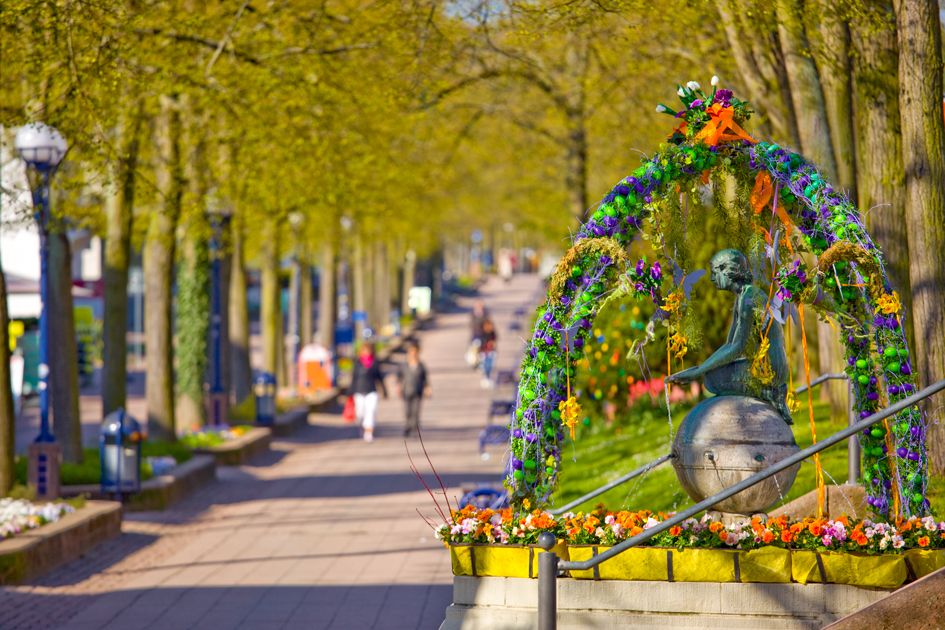 Bad Wildunger Osterschmuck auf der Brunnenallee. Im Fokus vorne rechts ist der bunt dekorierte Nymphenbrunnen zu sehen. Im Hintergrund die Linden der Brunnenallee und ein paar Fußgänger.