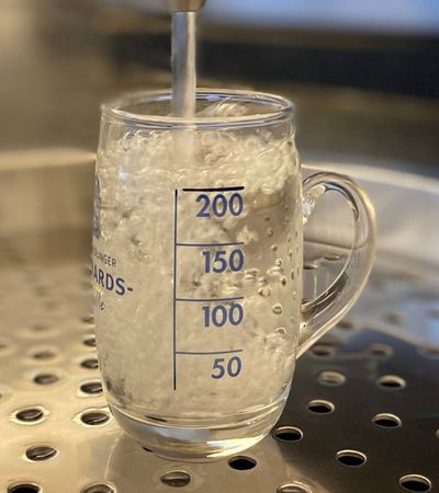 Bad Wildunger Trinkkurglas in Nahaufnahme, in das gerade Heilwasser eingegossen wird.