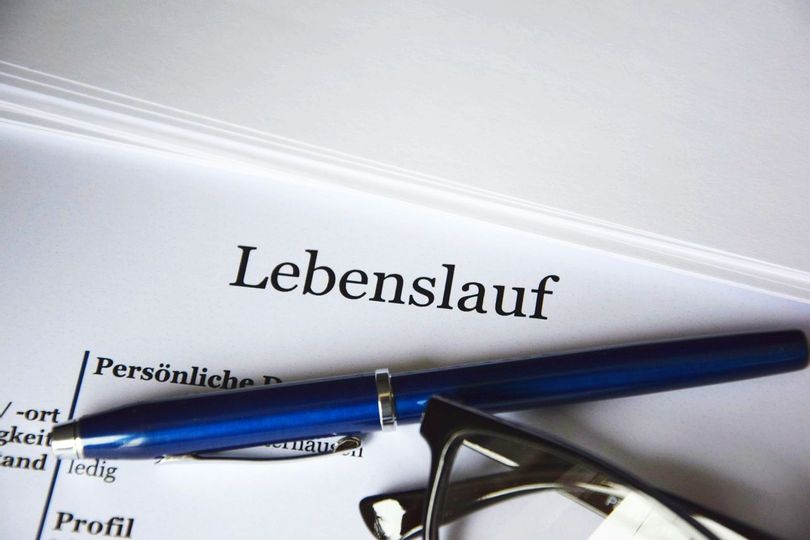 Nahaufnahme von einem Papier mit dem Titel "Lebenslauf". Auf dem Papier liegt ein Stift und eine Brille.