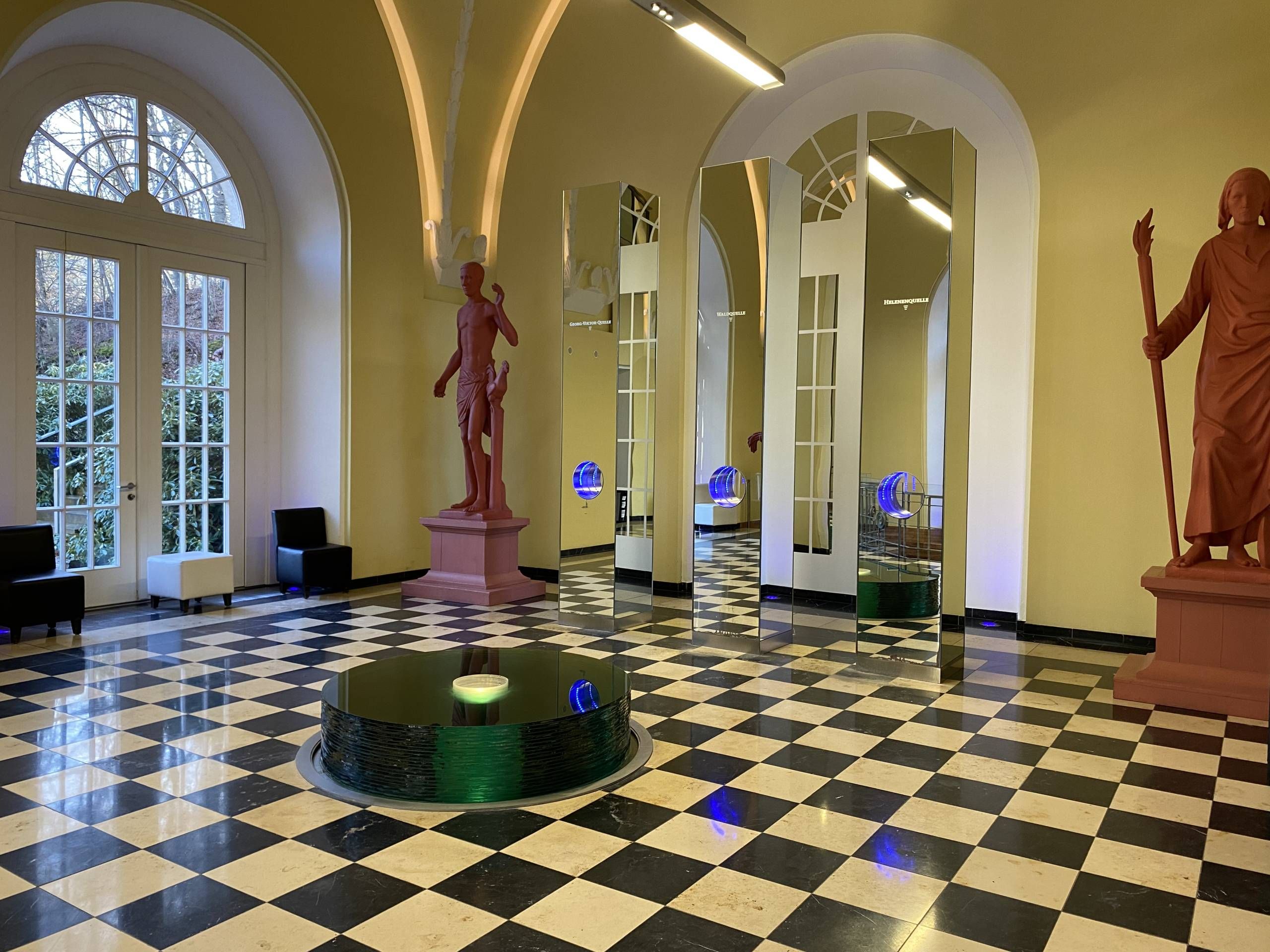 Blick in der Quellendom mit kleinem Brunnen, zwei roten Statuen und drei Zapfanlagen.